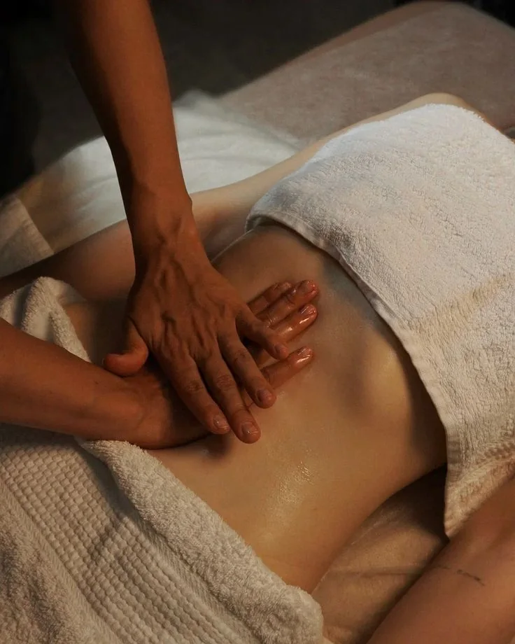 Illustrative photograph of hands massaging an abdomen beside white towels.